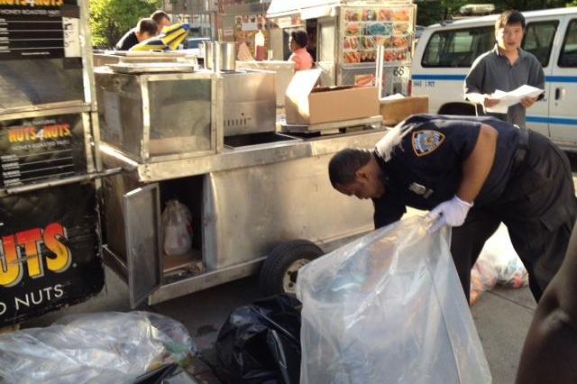 An NYPD officer empties a confiscated food cart taken from Broadway yesterday